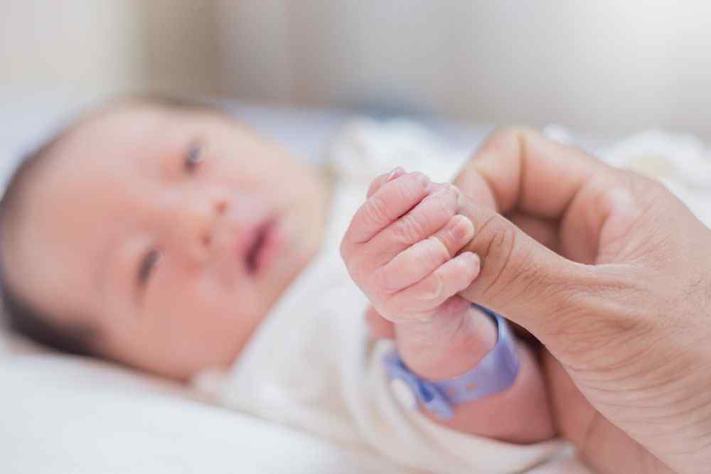 Yeni doğmuş bir bebek, bir yetişkinin parmağını tutuyor
