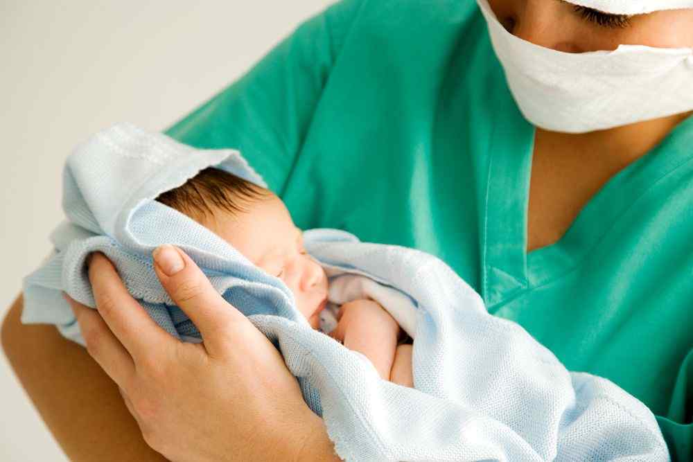 Maske takan sağlık çalışanı, battaniyeye sarılı yeni doğmuş bir bebeği kucağında tutuyor