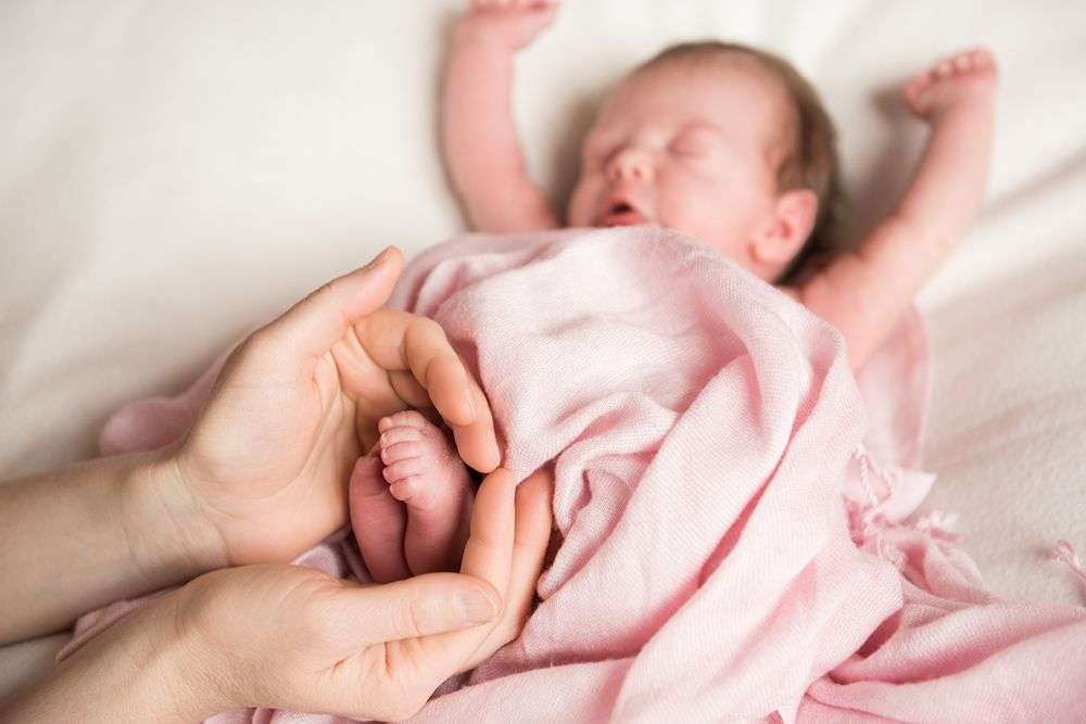 sunnet (36) Pembe battaniyeye sarılı uyuyan bebeğin ayaklarını yetişkin elleri tutuyor