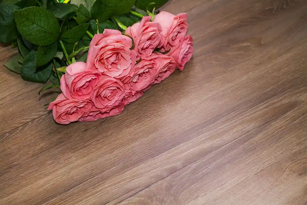 Ahşap masa üzerinde duran pembe güller ve yeşil yapraklar