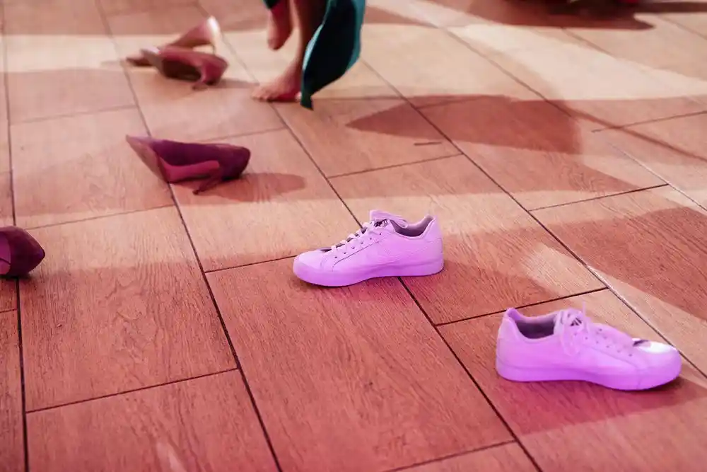 Ahşap zeminde dağınık halde duran pembe spor ayakkabılar ve topuklu ayakkabılar
