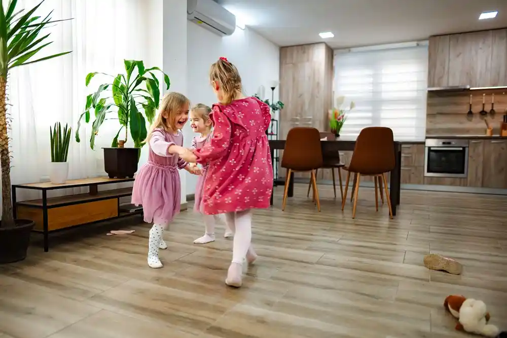 blog (173) Modern bir evin oturma alanında el ele tutuşarak dönen üç kız çocuğu