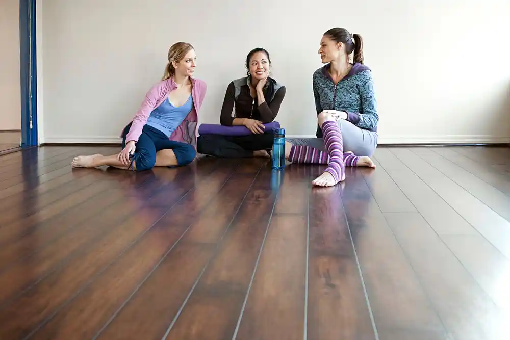 blog (174) Ahşap zeminde oturan üç kadın, yoga dersine başlamadan önce sohbet ediyor