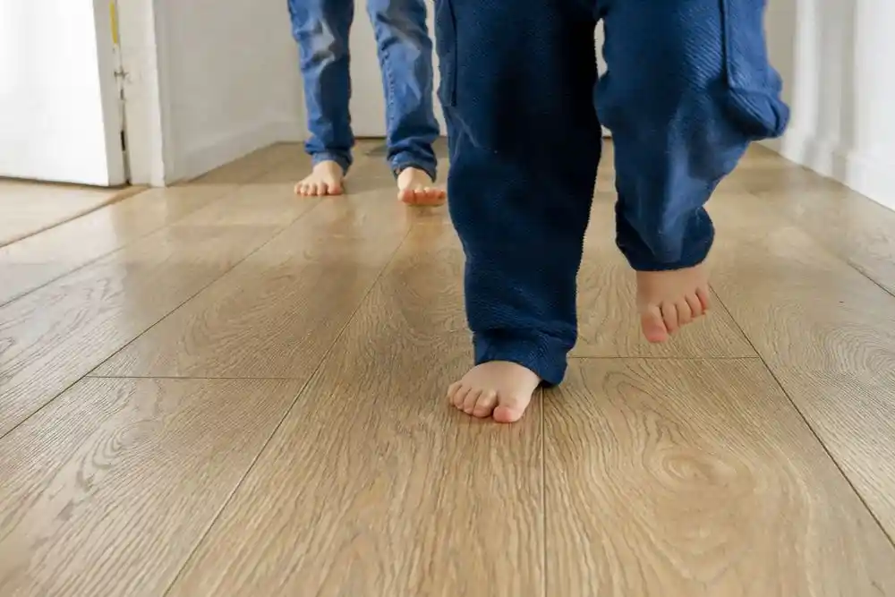 Mavi pantolonlu iki çocuk, ahşap zeminde yalınayak yürüyor
