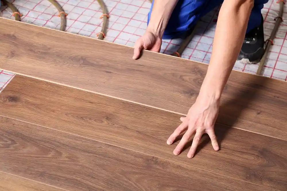 Bir kişi ahşap görünümlü laminat parke panellerini zemine yerleştiriyor